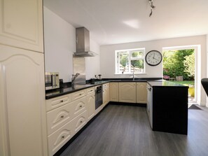 A modern kitchen with white cabinetry, a black countertop, a built-in oven, and a window with a view of greenery.