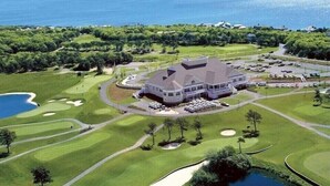 Een golfbaan met een clubhuis, een groot waterlichaam en een parkeerplaats.