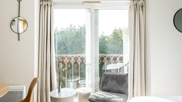 Een kamer met een bed, een stoel, een tafeltje, een spiegel en een balkon met een hekwerk.