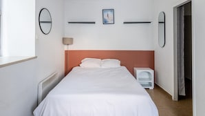 Een slaapkamer met een bed, een plafondlamp, een radiator en een raam.