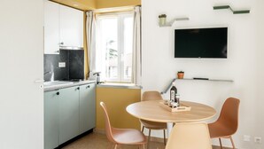 Een moderne keuken met een eethoek, een aan de muur bevestigde televisie en een raam met gordijnen.