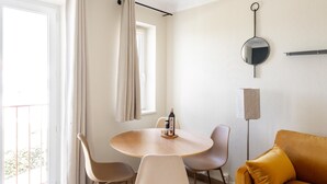 A modern living room with a round dining table, two chairs, a sofa, a small cactus plant, a hanging light fixture, and a window with curtains. - Studio Standard (Saint-Jean-de-Luz)