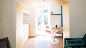 Ein modernes Wohnzimmer mit einer Couch, einem Glastisch, einem Essbereich mit Stühlen und einer durch einen Bogen sichtbaren Küche.