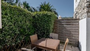Eine Terrasse im Freien mit Tisch und Stühlen, einem Holzzaun und einer Hecke.