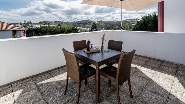 Un patio con una mesa, sillas y un gran paraguas, con vistas a un paisaje lejano.