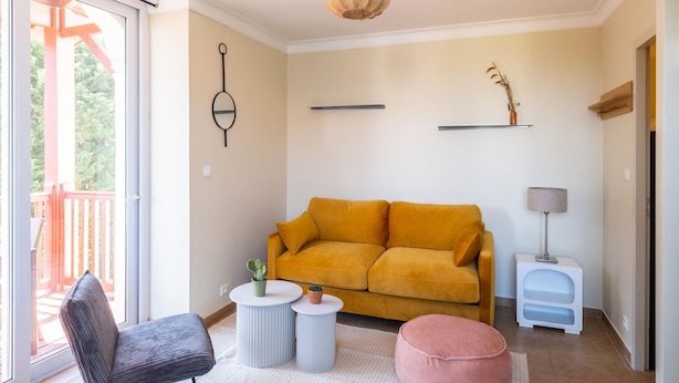 Ein Wohnzimmer mit einer Couch, einem Sessel, einem runden Hocker, einer Lampe und einer Pendelleuchte.