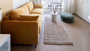 Ein modernes Wohnzimmer mit einer Couch, einem runden Hocker, einem kleinen Tisch und einer Deckenleuchte.