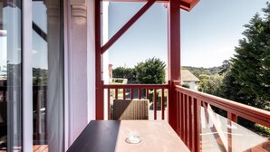 Ein überdachter Balkon mit Tisch und Korbstühlen, mit Blick auf eine reizvolle Landschaft.