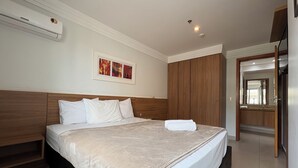 Ein Hotelzimmer mit Bett, einem hölzernen Kopfteil, einem gerahmten Bild an der Wand und einem durchgegangene Tür erkennbaren Badezimmer.
