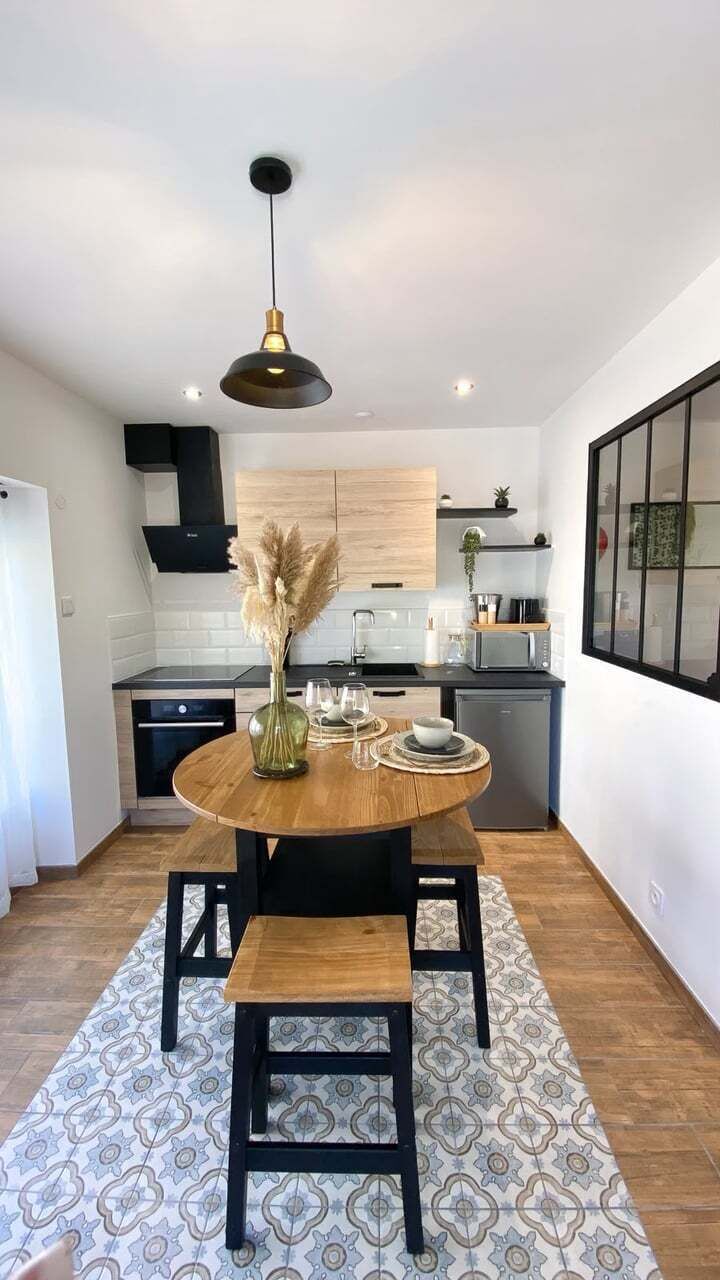 Uma cozinha moderna com uma mesa de madeira redonda, cadeiras pretas e uma luminária pendente.