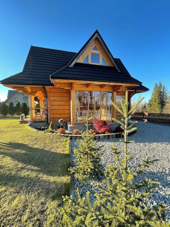 A log cabin with a sloped roof, a porch, and a gravel driveway.