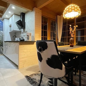 A dining area with a wooden table, a black and white patterned chair, a vase with flowers, and a pendant light.