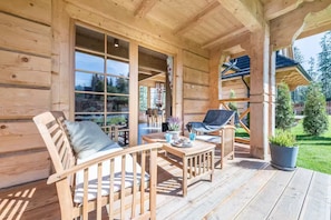 A wooden cabin with a covered porch, two wooden chairs, a table, and a potted plant.