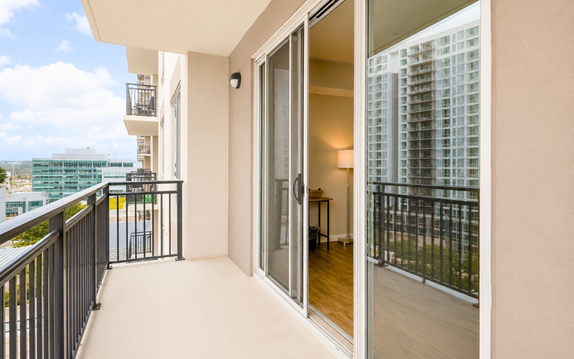 A balcony with a view of a cityscape, a sliding glass door, and a small table with a lamp.