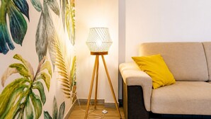 Une pièce avec un canapé, une lampe sur pied et un mur décoré d’une fresque représentant des plantes.