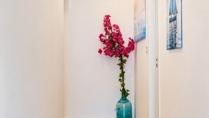 Un couloir au sol recouvert de planches de bois, un vase rempli de fleurs roses et deux tableaux accrochés au mur.