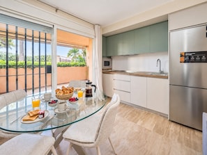 Een moderne keuken met een roestvrijstalen koelkast, een glazen eettafel met stoelen en uitzicht op groen.