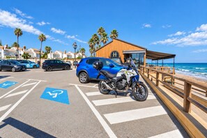 A parking area with a motorcycle, a blue car, and a building with a wooden facade. - GuestReady - Marbella vibes with pool (Marbella)