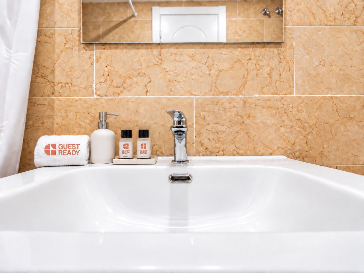 Een hotelbadkamer met een betegelde muur van marmer, een witte wastafel, een spiegel en toiletartikelen met de aanduiding 'Klaar voor gasten'.