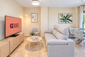 A modern living room with a flat-screen TV, a sofa, a coffee table, and a dining area with chairs. - GuestReady - Marbella vibes with pool (Marbella)