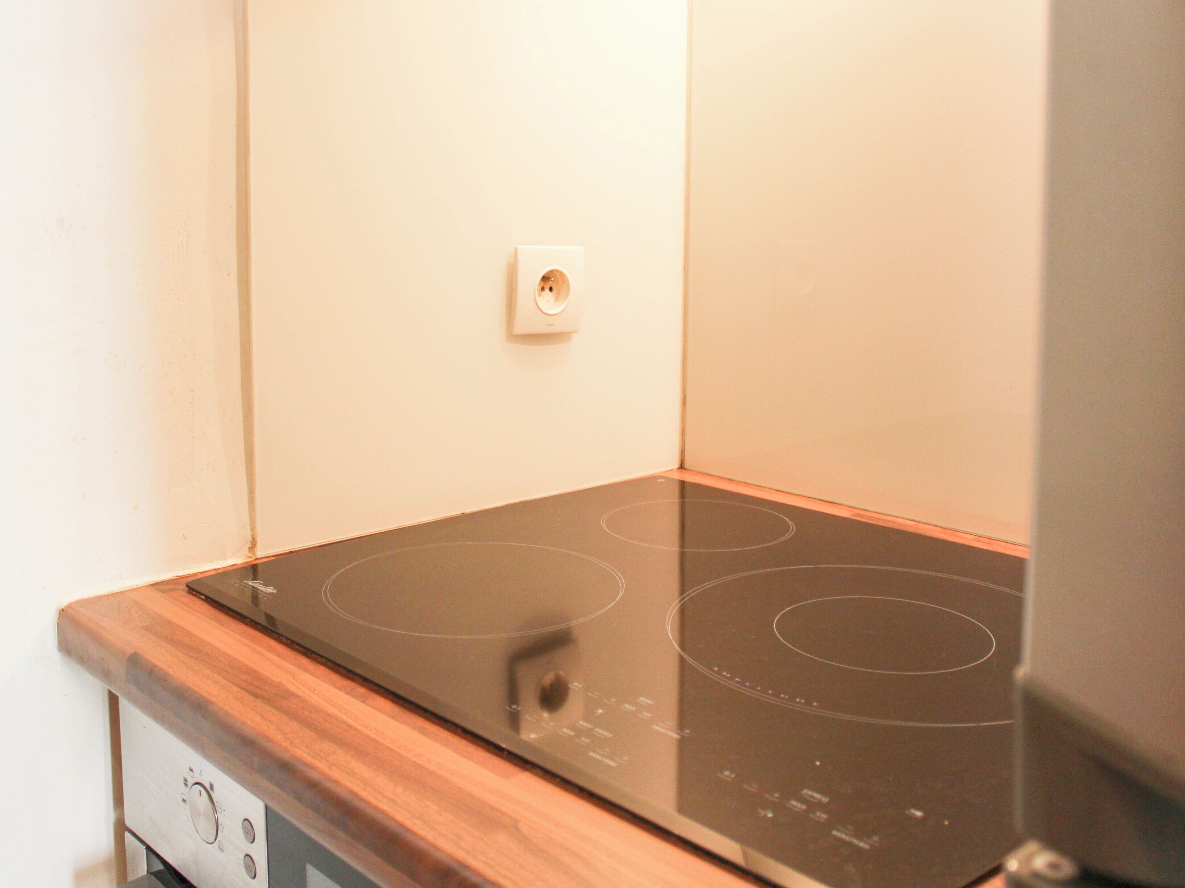 Une cuisine équipée d’une plaque de cuisson à induction, d’un plan de travail en bois et d’une prise électrique murale.