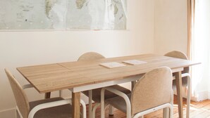 Uma sala de jantar com mesa de madeira e quatro cadeiras, um mapa-múndi na parede e uma luminária pendente.