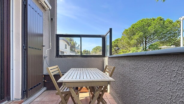 Eine Terrasse mit Holztisch und -stühlen, einem Fenster und einer Tür.