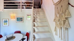 Eine Treppe mit Wandbehang aus Makramee, gerahmten Bildern an der Wand und einem Essbereich mit Tisch und Stühlen.