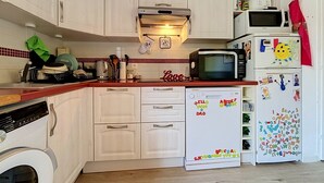 Eine Küche mit weißen Schränken, einem Geschirrspüler, einer Mikrowelle und einem Kühlschrank mit Kinderzeichnungen.