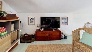 Ein Wohnzimmer mit Fernseher, Holzmöbeln, einem Korbsessel und einem kleinen Hundebett.