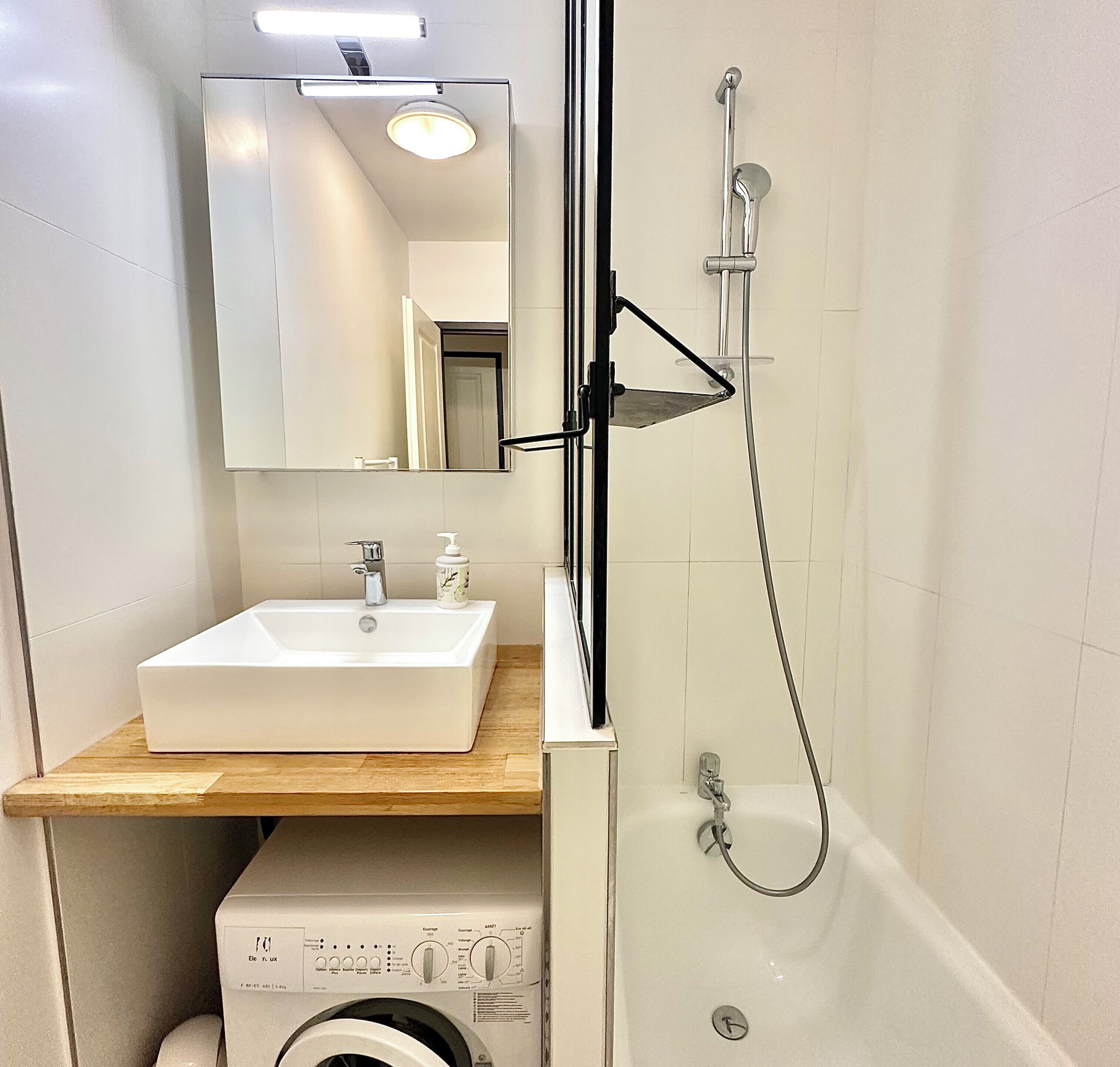Ein Badezimmer mit Waschbecken, Spiegel, Dusche und Waschmaschine.