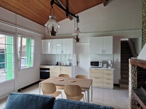 Eine moderne Küche mit weißen Schränken, ein Essbereich mit einem Holztisch und Stühlen sowie eine Treppe, die in einen oberen Bereich führt.