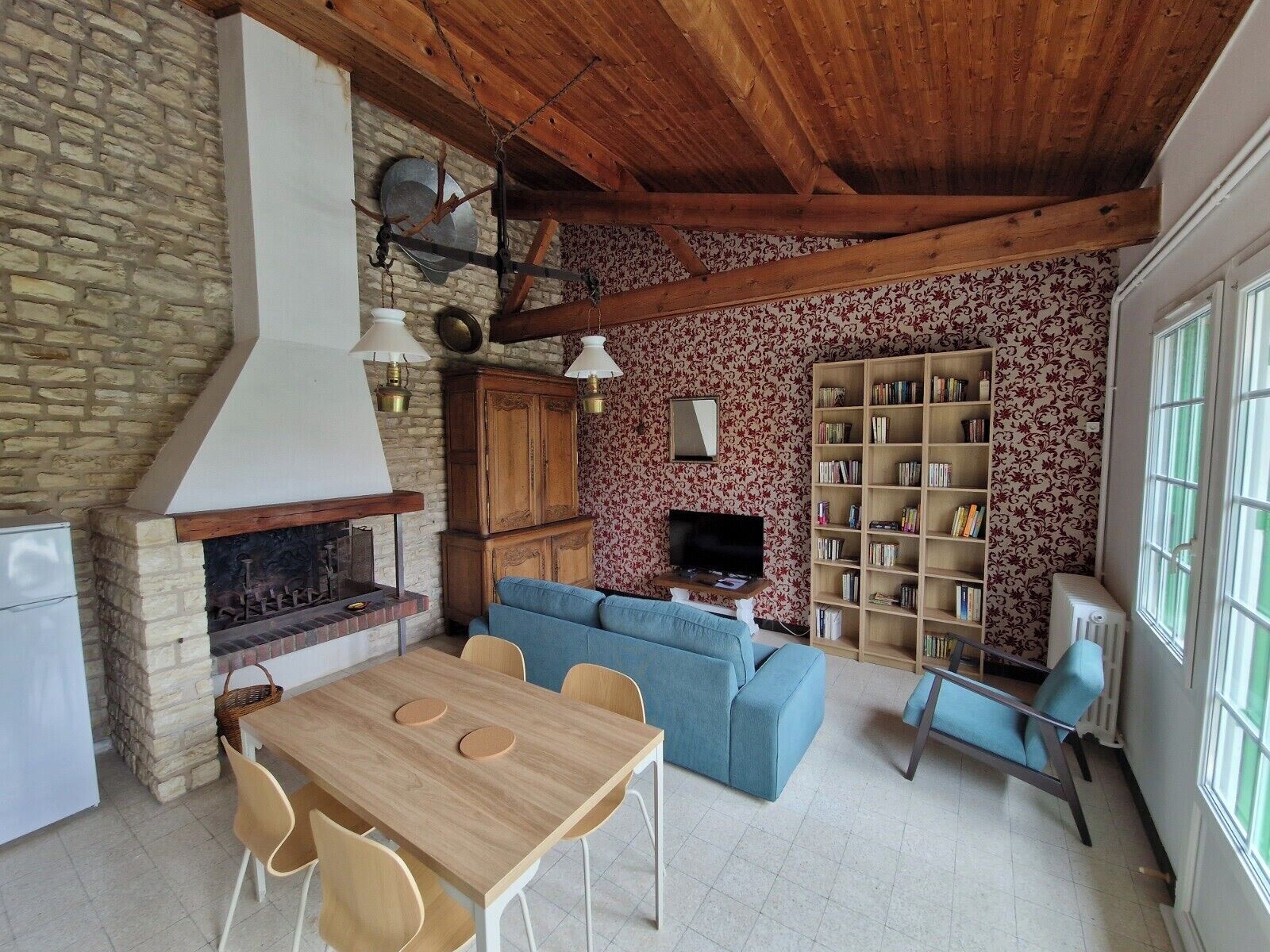 Un intérieur rustique avec une cheminée en pierre, une table à manger en bois, un canapé bleu et une bibliothèque.
