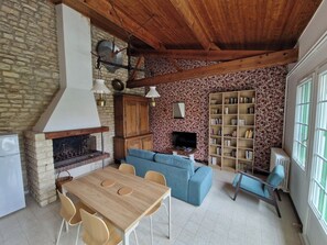 Ein rustikales Interieur mit Kamin aus Stein, einem Holztisch, einem blauen Sofa und einem Bücherregal.