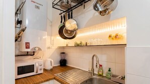 Een keuken met een magnetron, broodrooster, spoelbak en hangende pannen.