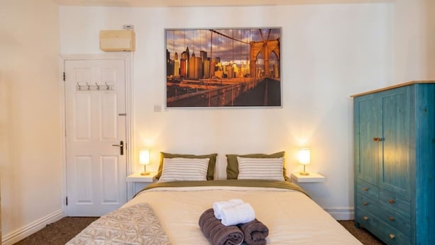 Een hotelkamer met een bed, twee bedlampen, een stadsgezicht schilderij boven het bed, een deur en een blauwe kast.