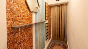 Een gang met een bakstenen muur, een plank, een klok en een deur voorzien van gordijnen.