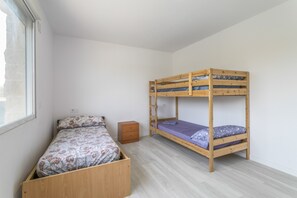 A room with a bunk bed, a single bed, a small wooden dresser, and a window.