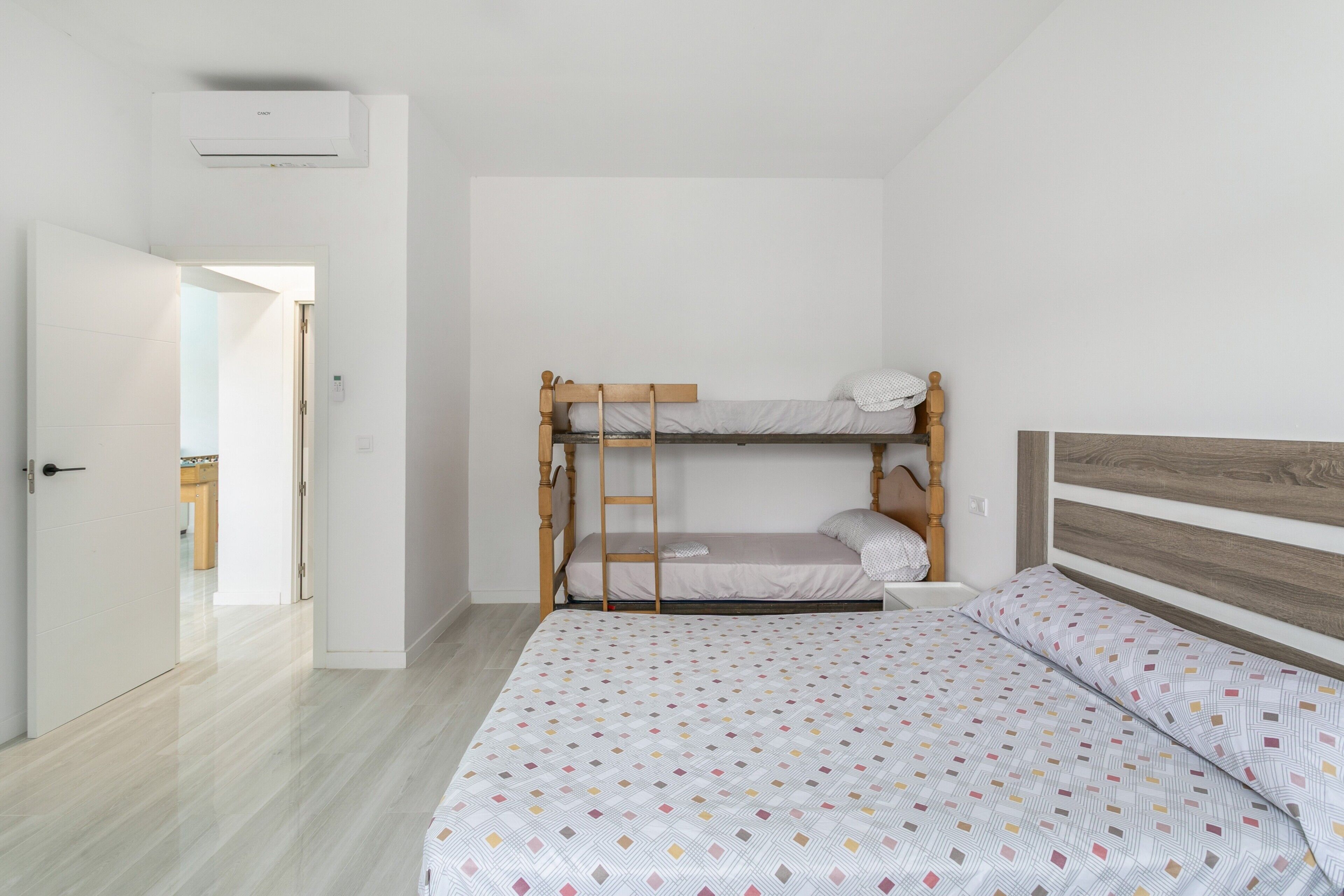 A bedroom with a bunk bed, a single bed, and a door leading to another room.