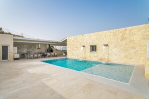 A swimming pool with a stone wall, outdoor seating, and a covered area with a grill. - Villa 'Bender House' with Mountain View, Wi-Fi and Air Conditioning (Urbanización Villanueva)