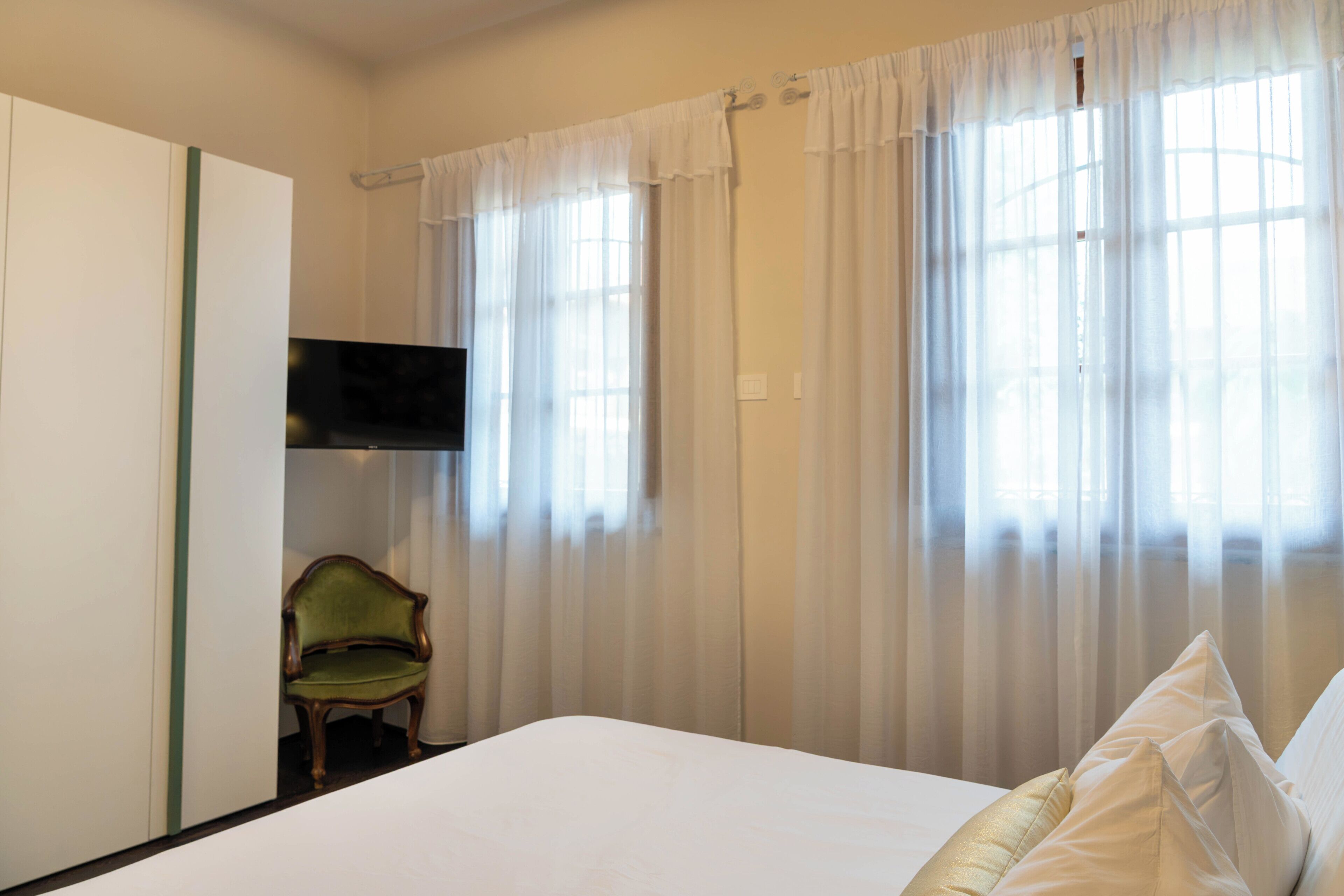 A bedroom with a bed, a chair, a television, and sheer curtains.