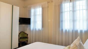 A bedroom with a bed, a chair, a television, and sheer curtains.