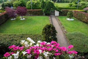 A well-maintained garden with a paved pathway leading to a small building, surrounded by neatly trimmed hedges and flowering plants.