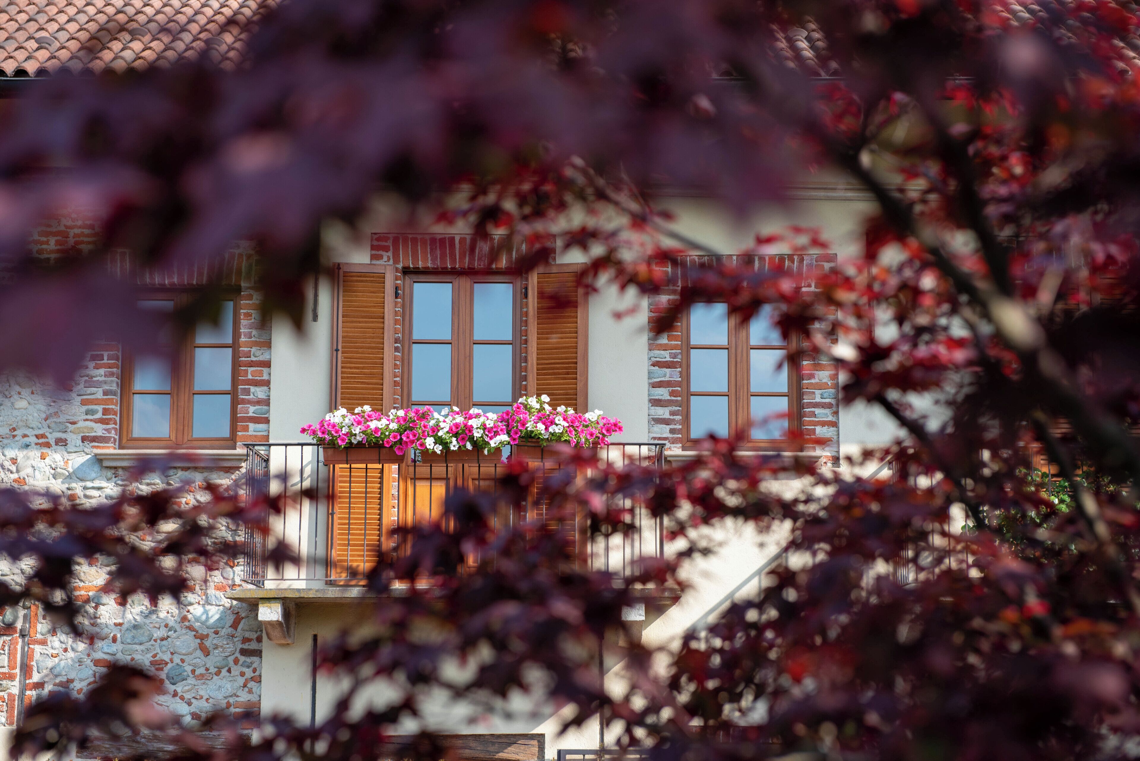 A building with a brick facade, wooden shutters, and a balcony with flower boxes.