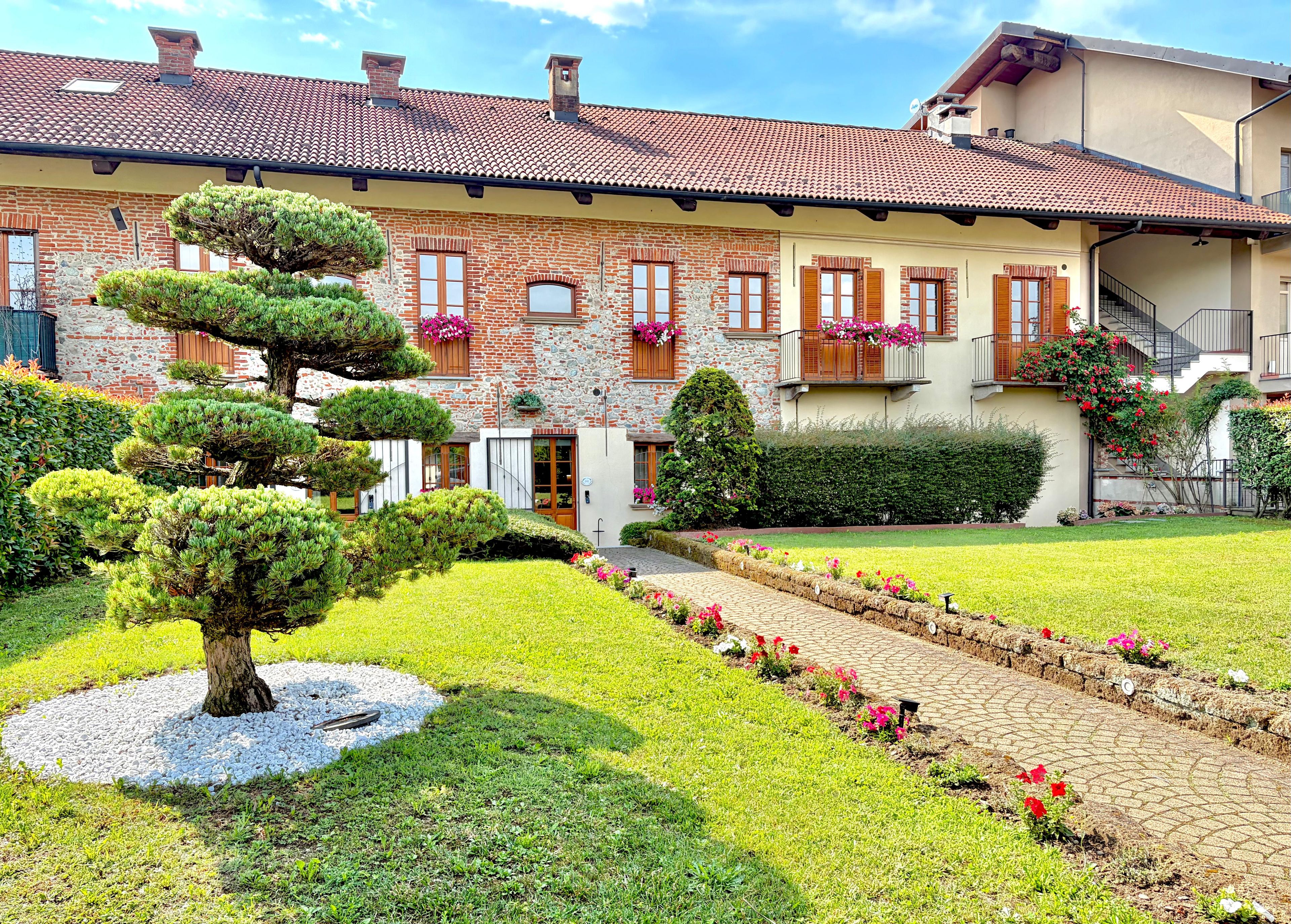 A two-story building with a brick facade, a tiled roof, and a well-maintained garden with hedges and flower beds.