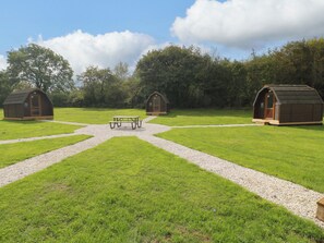A campsite with three wooden cabins, a picnic table, and gravel paths.