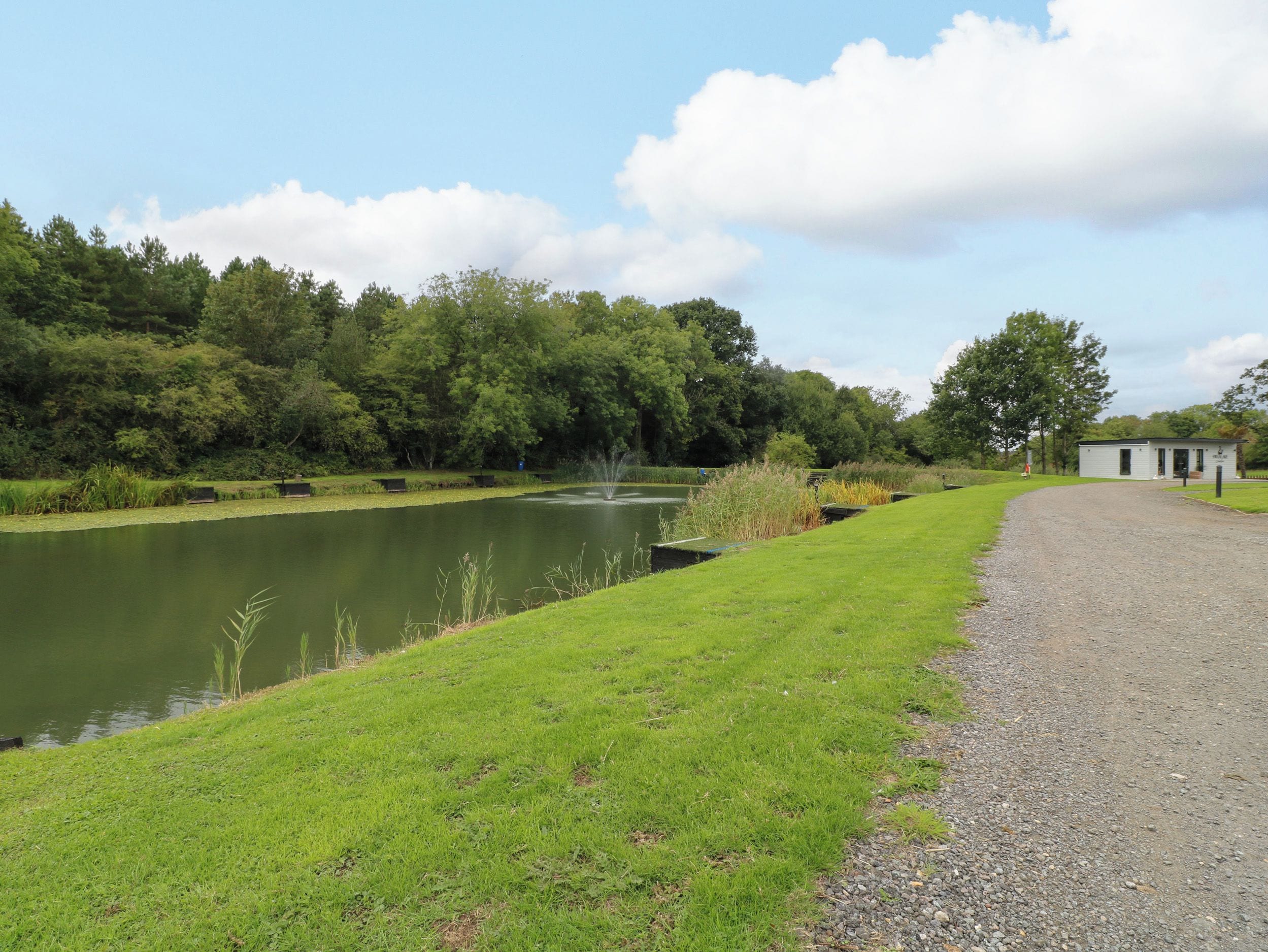A tranquil outdoor setting with a pond, grassy areas, and a small building, likely a facility or rest area.
