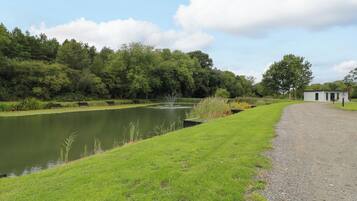 A tranquil outdoor setting with a pond, grassy areas, and a small building, likely a facility or rest area.