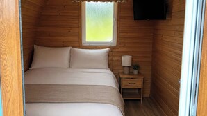 A small, cozy room with a bed, a nightstand, a lamp, and a window.