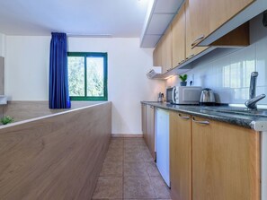 A modern kitchen with wooden cabinets, a microwave, a kettle, and a window with blue curtains. - Festival Village by Interhome (Salou)